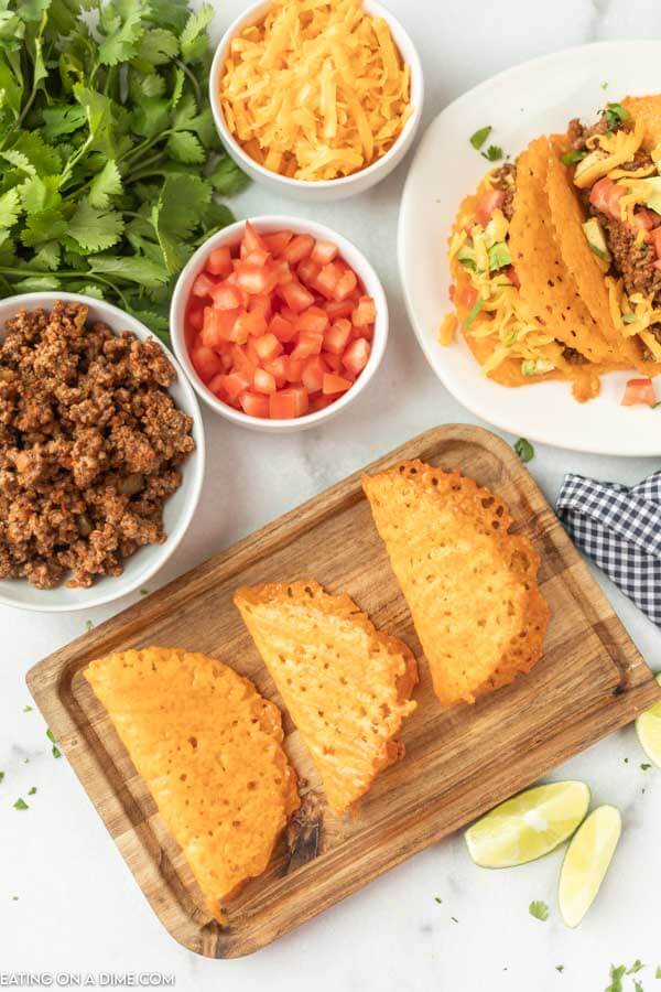 Close up image of keto taco shells on a cutting board with a side of hamburger meat, tomatoes