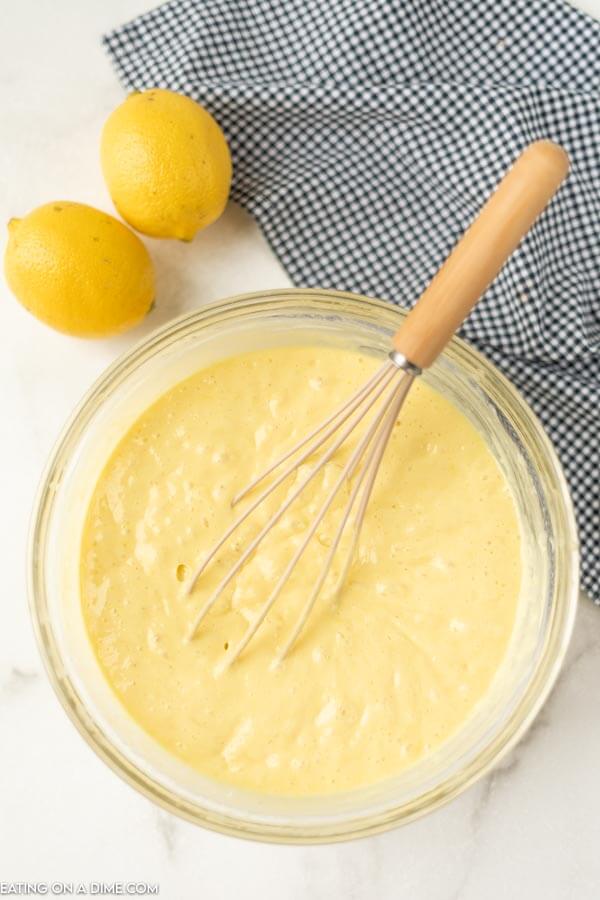 Close up image of lemon cupcake batter being mixed in a clear bowl with a whisk.