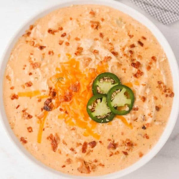 Bowl of jalapeno popper soup topped with shredded cheese and slice jalapenos.