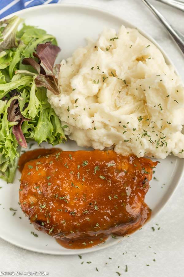 Close up image of pork chops covered in marinade with a side of mashed potatoes and salad on a white plate. 