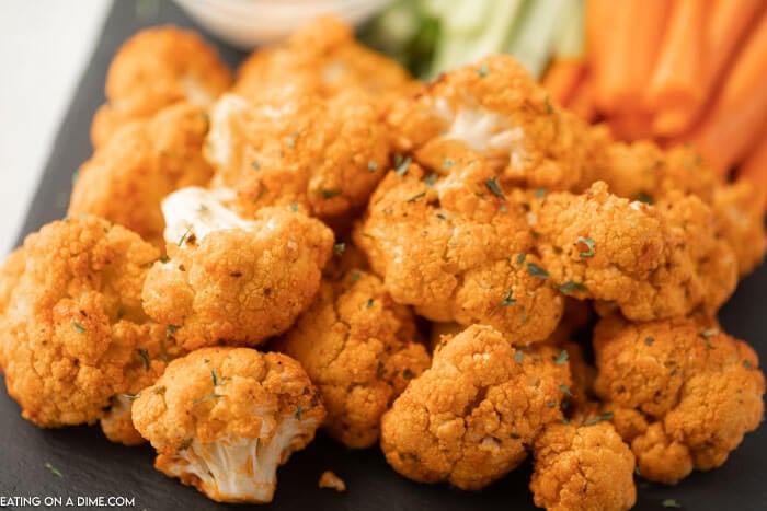 Close up image of buffalo cauliflower on a serving tray with ranch dip and carrots and celery. 