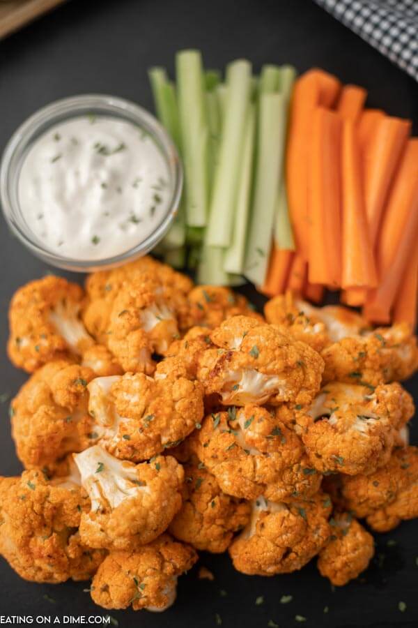 Close up image of buffalo cauliflower on a serving tray with ranch dip and carrots and celery. 