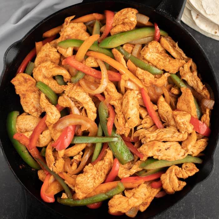 Cast iron skillet of chicken strips, bell peppers and onion. 