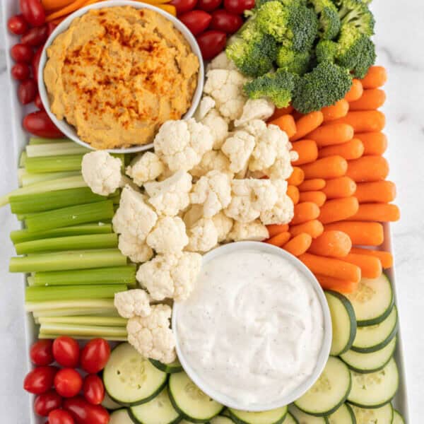 Veggie tray with cherry tomatoes, cucumbers, baby carrots, cauliflower, broccoli, orange and red bell peppers, celery, hummus and ranch dip.