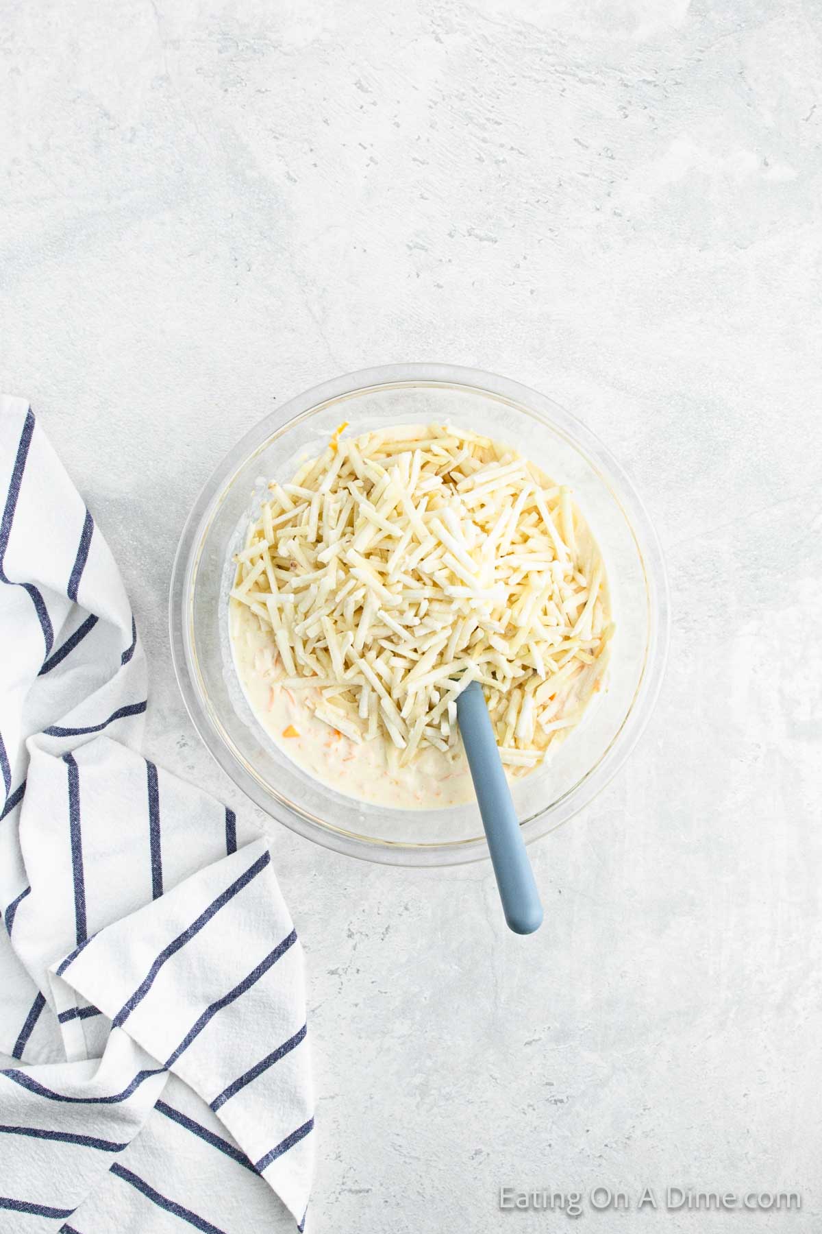 Adding in shredded hashbrowns in the sour cream mixture in a bowl