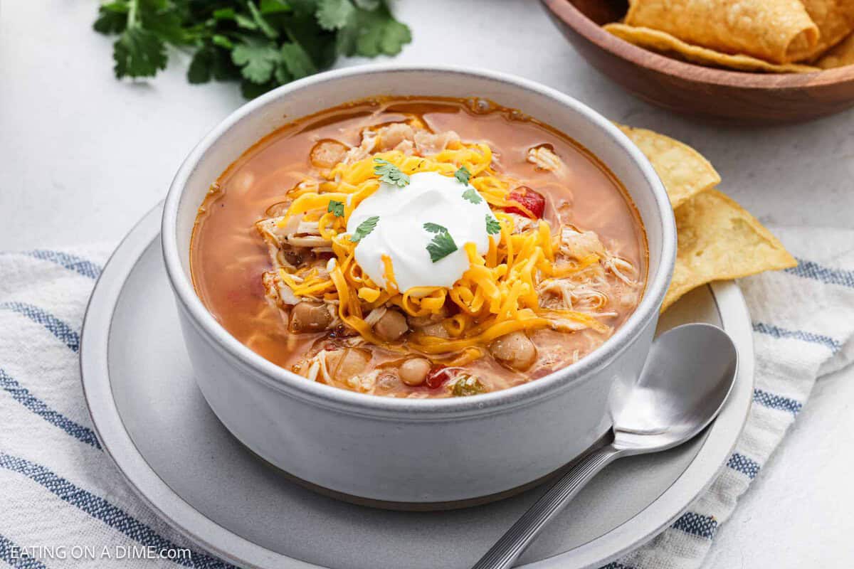 Chicken Taco Soup in a white bowl topped with shredded cheese and sour cream with a side of tortilla chips.