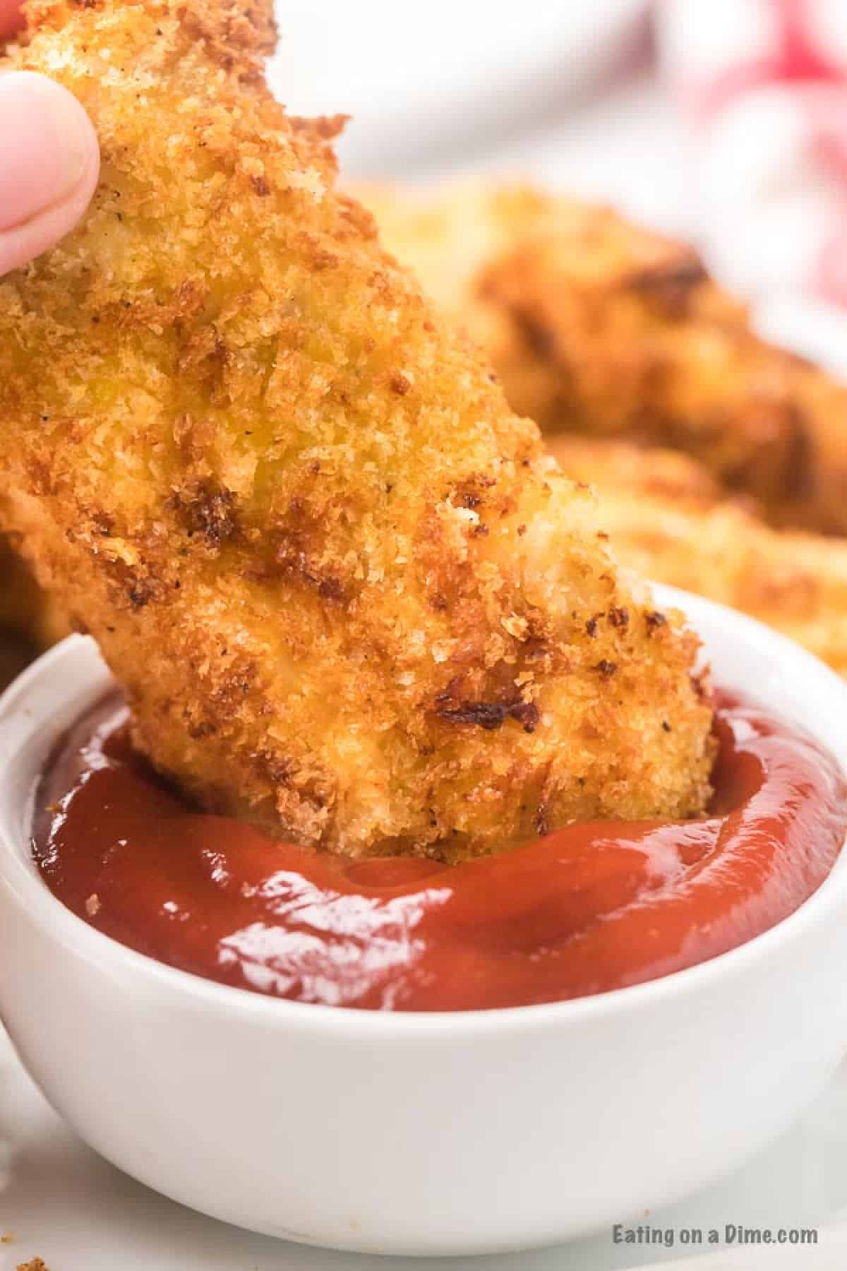 Closeup of air fryer chicken tender dipped in ketchup.