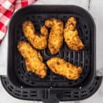 Five crispy air fryer chicken tenders inside an air fryer basket.