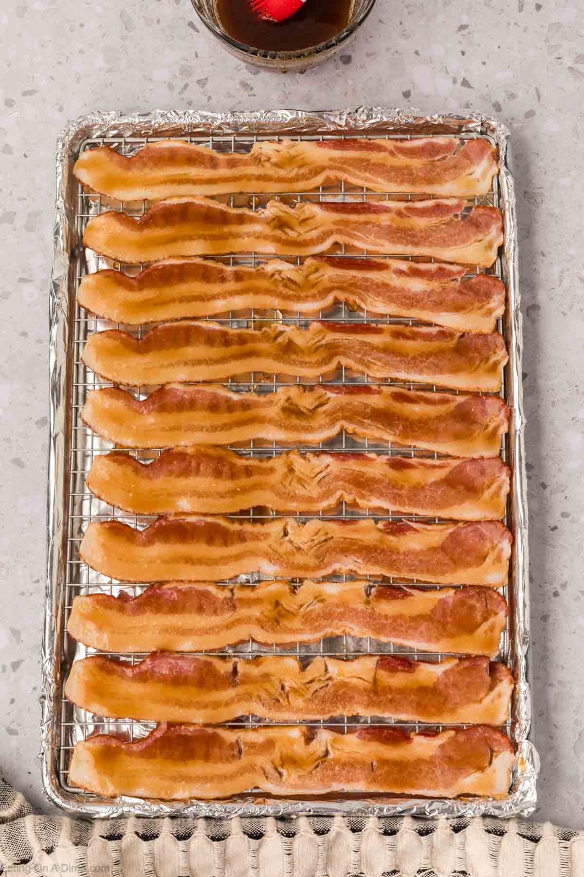 A baking sheet lined with foil holds several strips of candied bacon, arranged neatly in rows on a wire rack—perfect for anyone searching for an easy candied bacon recipe.