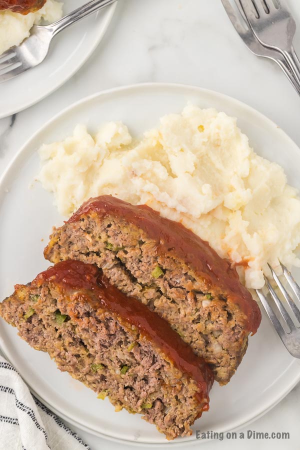 Close up image of two slices of meatloaf on a white plate with a side of mashed potatoes. 