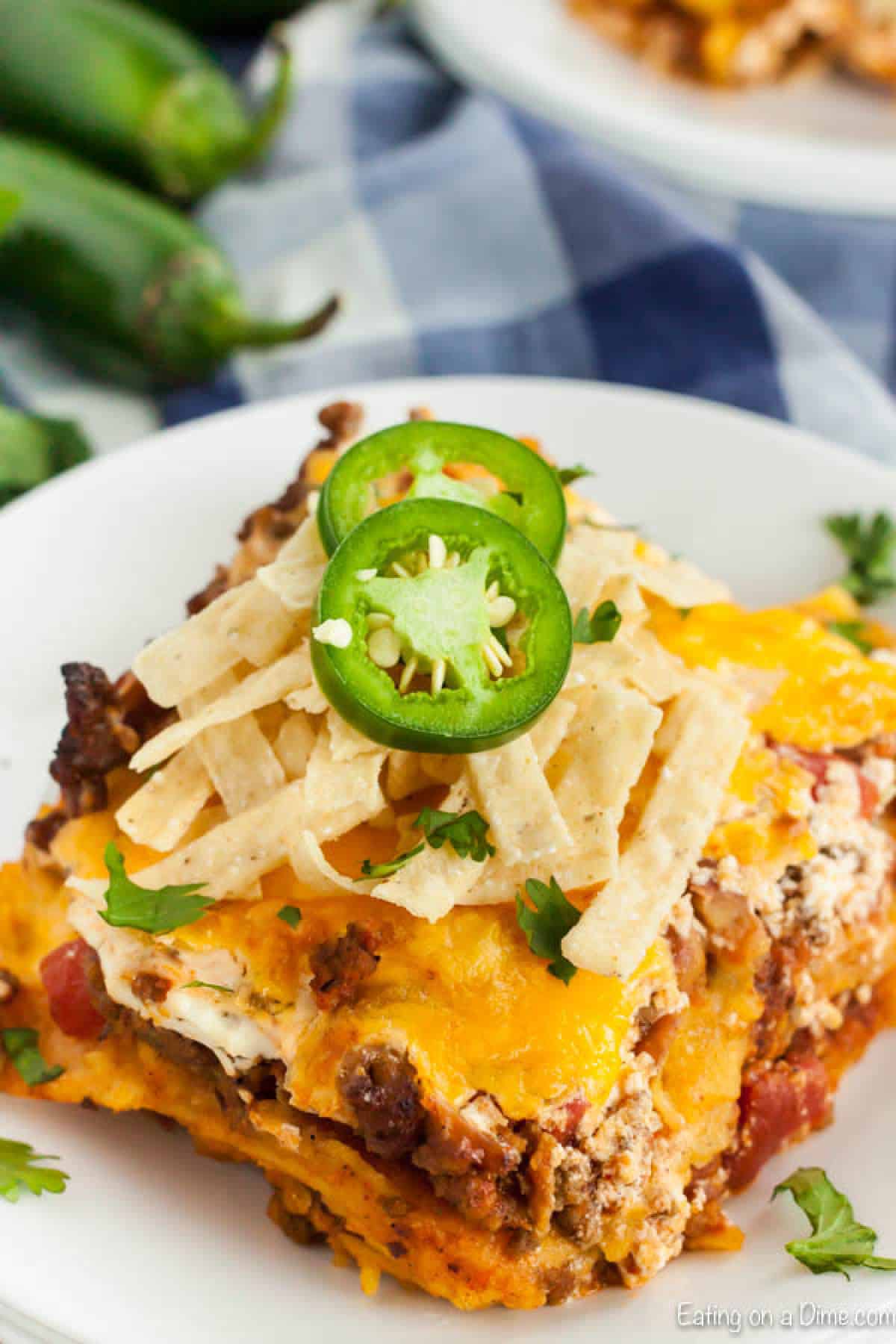 Easy Mexican Casserole Recipe has the most delicious layers of cheese, ground beef, tortillas and more. This casserole is perfect any day of the week. A piece of this Mexican casserole on a plate topped with tortilla strips and sliced jalapeรฑos.