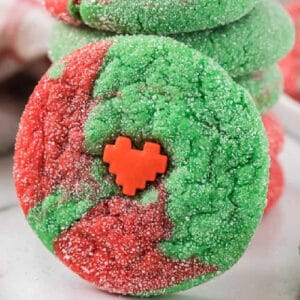A round cookie with red and green swirled dough, coated in sugar, and topped with a small red heart-shaped decoration in the center—just like a classic Grinch cookies recipe.