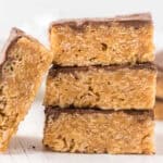 Three stacked Scotcheroos Bars, featuring a peanut butter and chocolate crispy texture, with a fourth bar leaning against the stack—all set on a white surface.
