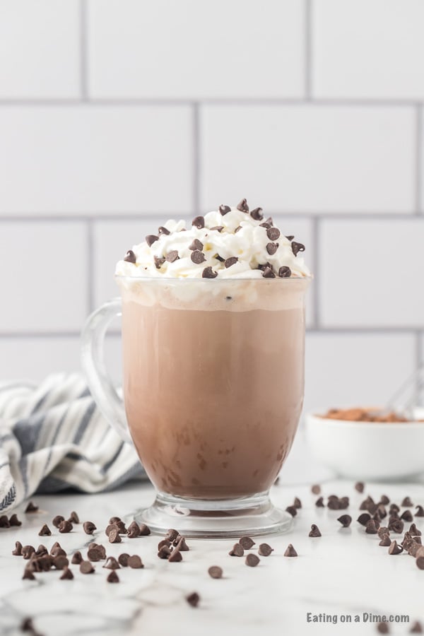 Clear mug with hot cocoa topped with whipped cream and chocolate chips. 