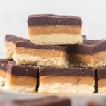 A close-up of stacked dessert bars with three layers: a crumbly shortbread base, a golden caramel middle, and a smooth chocolate top—just like the irresistible Homemade Twix Bars Recipe.