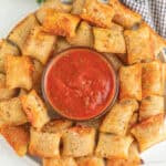 A plate of golden-brown air fryer pizza rolls arranged in a circle around a bowl of marinara sauce, ready for dipping.