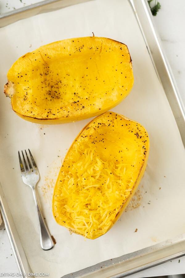 Close up image of cooked spaghetti squash on a baking sheet with a fork. 