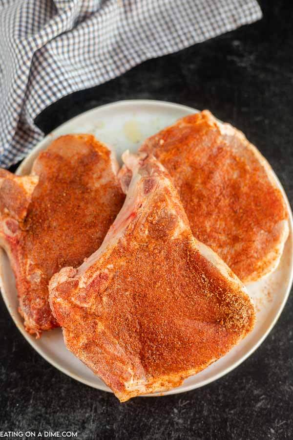 Close up image of uncooked pork chops on a plate with the seasoning rubbed on. 