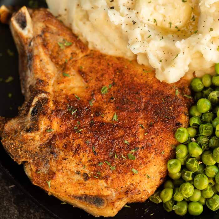 Close up image of bone-in pork chops with mashed potatoes and peas. 