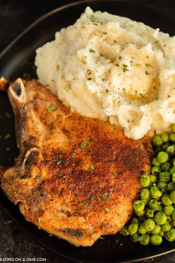 Close up image of bone-in pork chops with a side of mashed potatoes, and peas. 