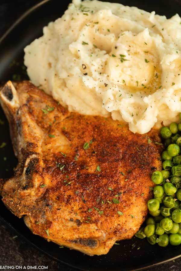 Close up image of pork chops on a plate with mashed potatoes and peas. 