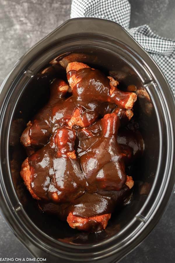 Close up image of drumsticks in a crock pot with BBQ sauce on top. 