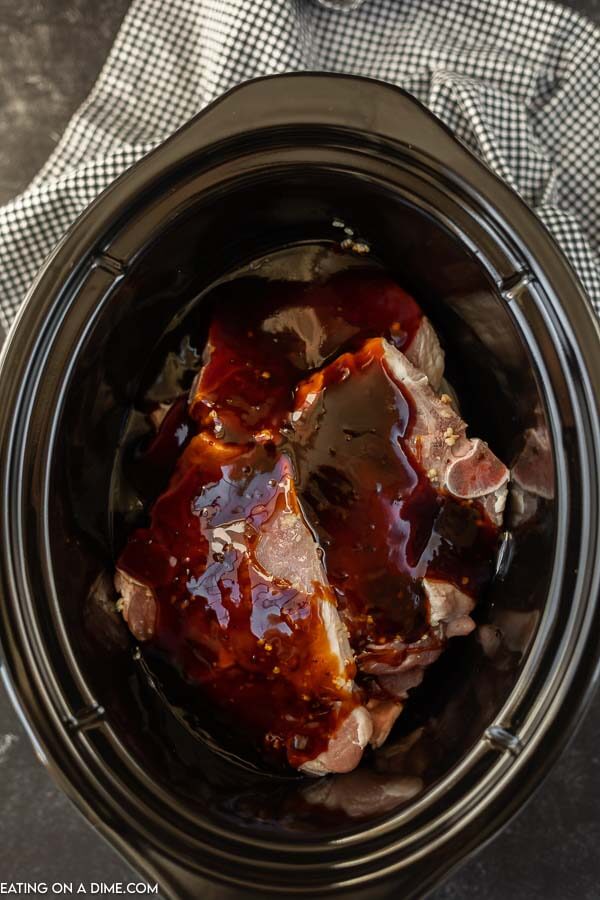 Close up image of uncooked pork chops in the crock pot with the teriyaki sauce over top. 