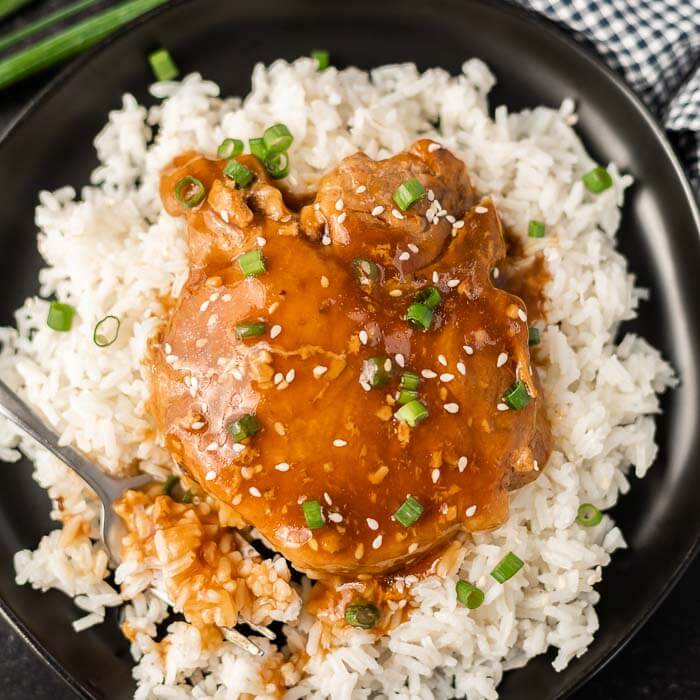Close up image of teriyaki pork chops on rice on a plate with a fork.