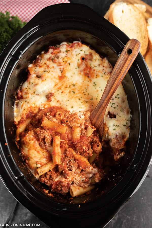 Slow cooker of baked ziti with a wooden spoon. 