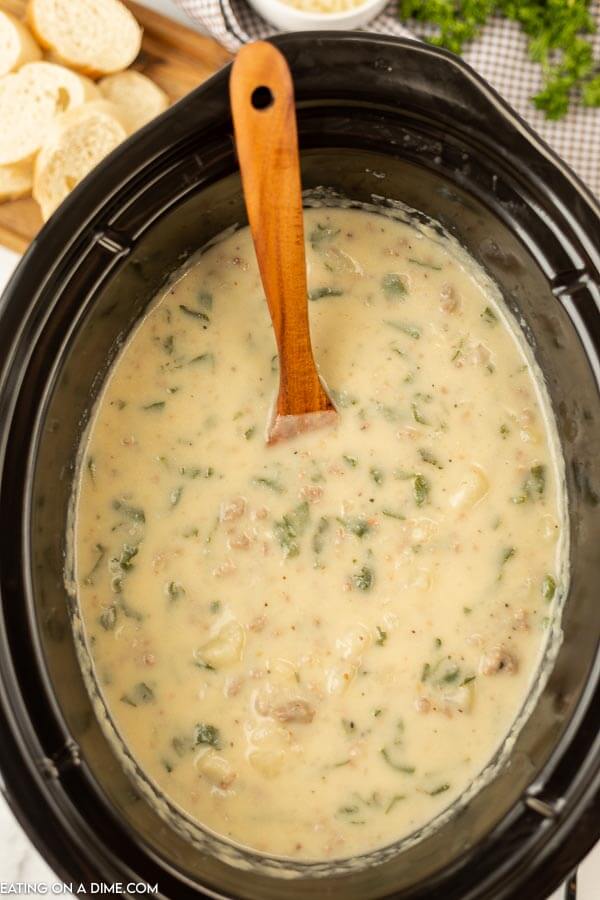 Close up image of Zuppa Toscana in a crock pot with a wooden spoon. 