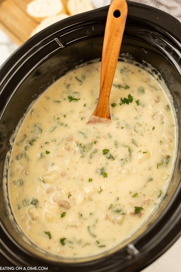 Close up image of Zuppa Toscana in crock pot with a wooden spoon.  