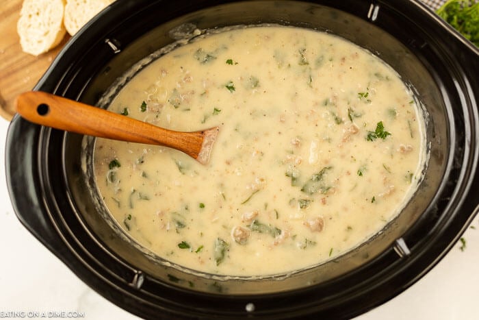 Close up image of Zuppa Toscana in a crock pot with a wooden spoon. 