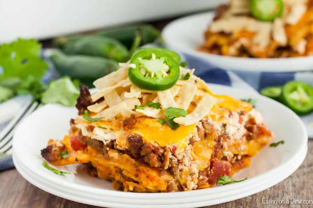 Easy Mexican Casserole Recipe has the most delicious layers of cheese, ground beef, tortillas and more. This casserole is perfect any day of the week. A piece of this Mexican casserole on a plate topped with tortilla strips and sliced jalapeños.