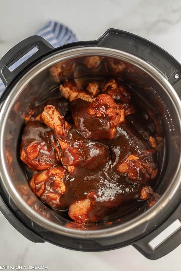 The chicken legs in the Instant Pot with the BBQ sauce poured over the top of the chicken legs 