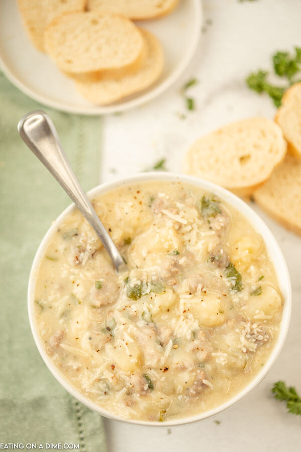Close up image of a white bowl of Zuppa Toscana Soup with a spoon and a side of bread. 