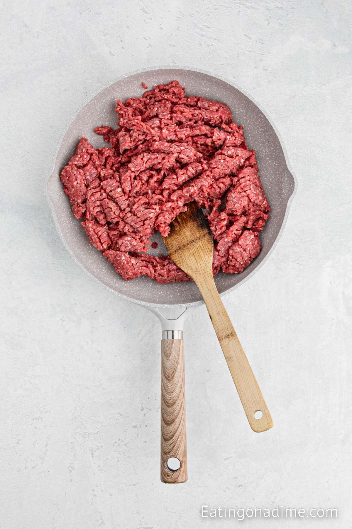 Cooking the ground beef in a skillet with a wooden spoon