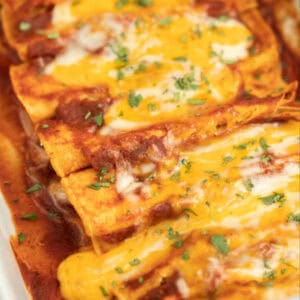 Close up of a cheese enchiladas in a baking pan topped with shredded cheese.