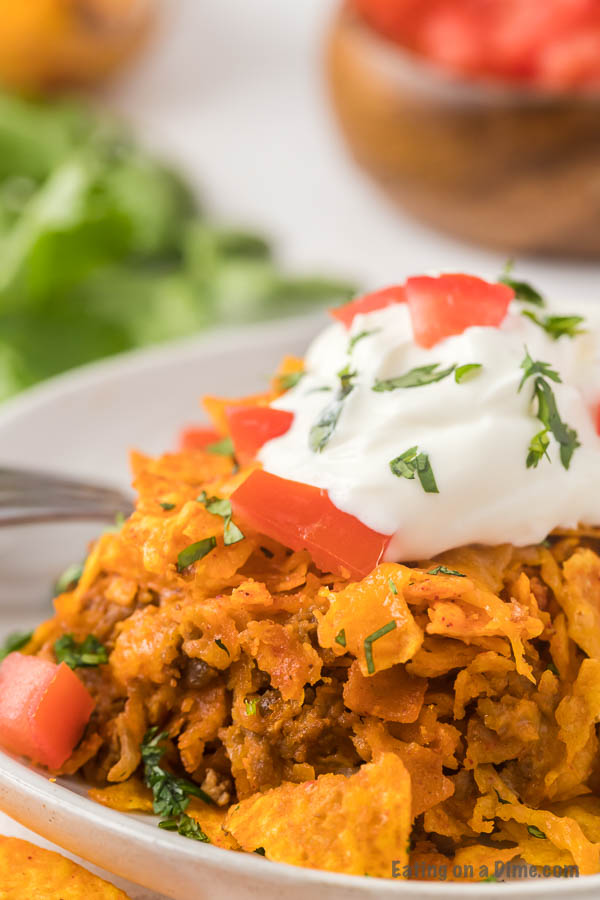 Close up image of Dorito Casserole on a white plate topped with tomatoes and sour cream. 