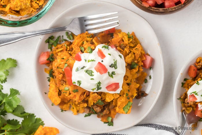 Close up image of Dorito Casserole on a white plate topped with tomatoes and sour cream. 