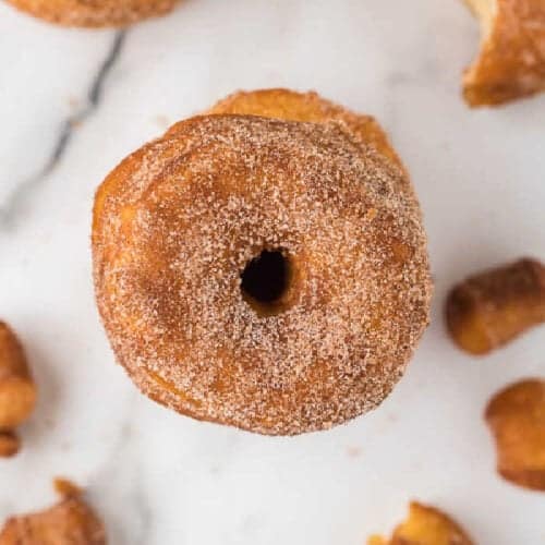 An overhead shot of a single doughnut with a dusting of cinnamon sugar on a marble surface. Other pieces of easy biscuit donuts are partially visible around it.