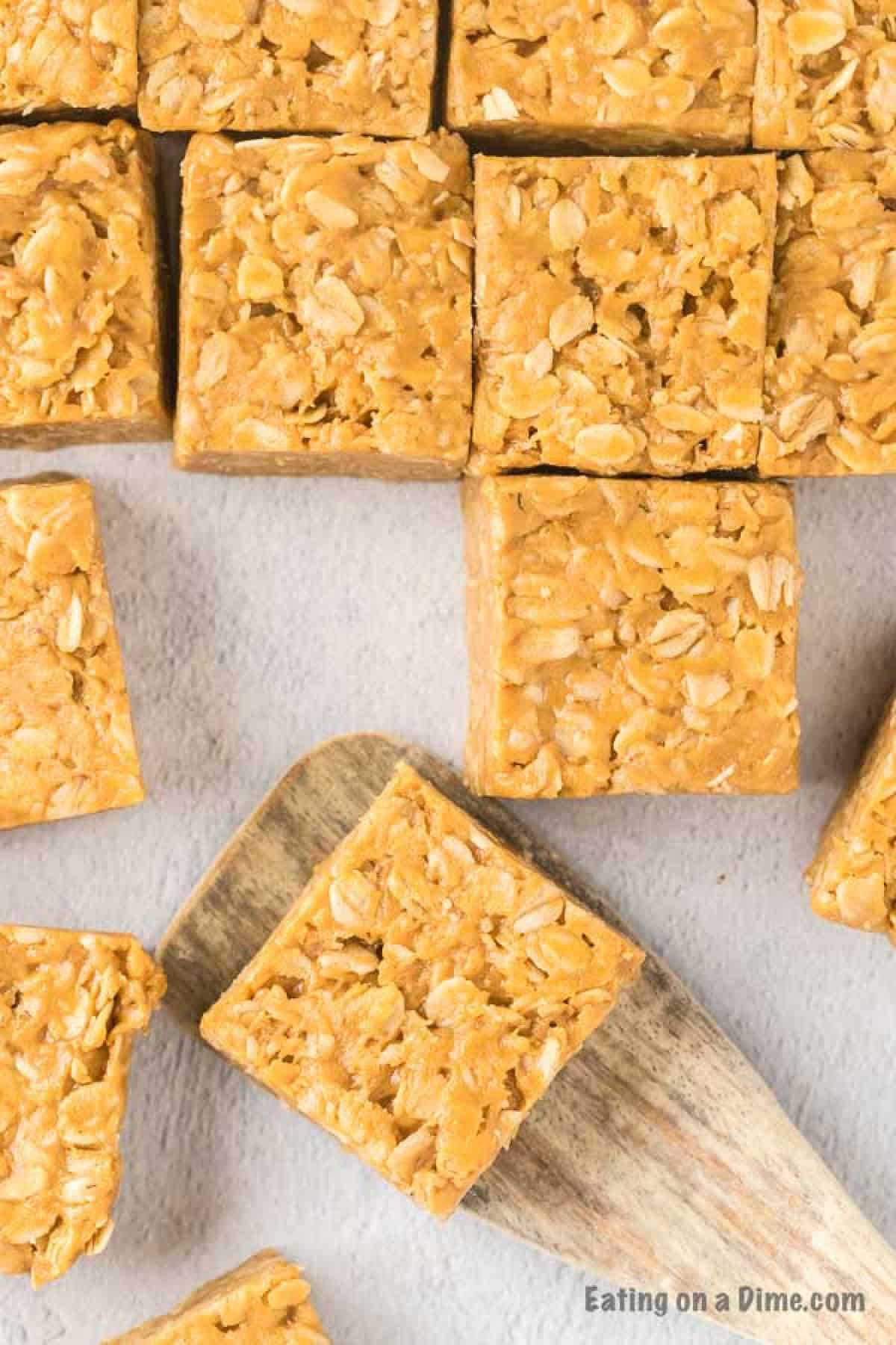 Close up image of Peanut Butter Oat Bars cut in serving size with a serving on a wooden spatula.