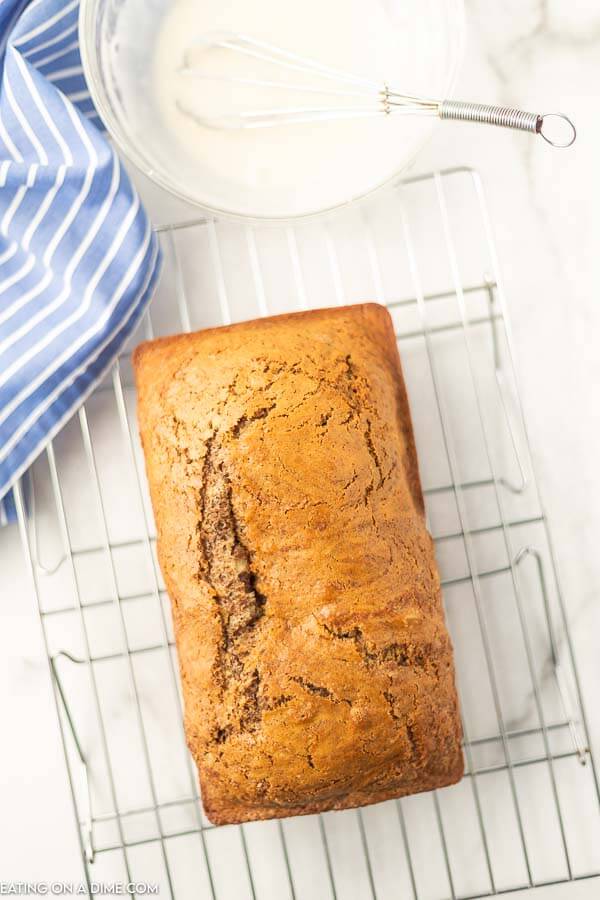 Close up image of cinnamon swirl bread on a cooling rack with a bowl of glaze with a whisk. 