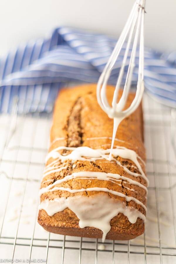 Close up image of cinnamon bread on a cooling rack with glaze being put on the bread with a whisk. 