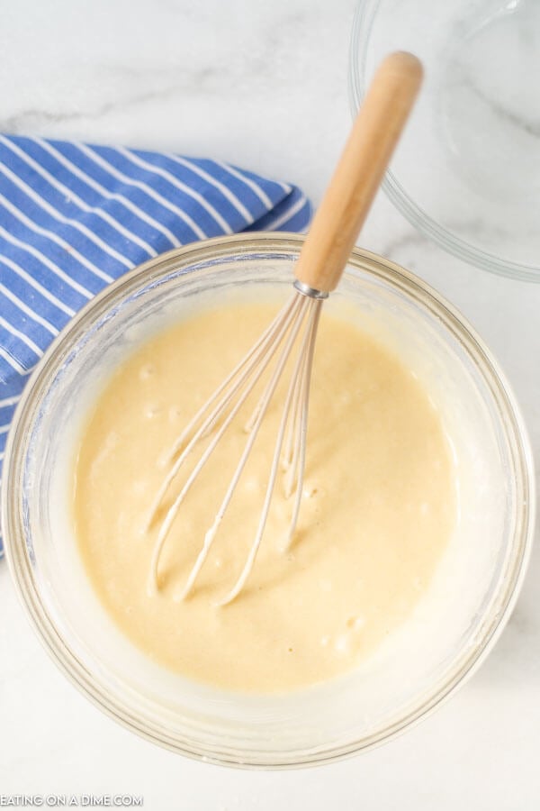 The process of mixing the bread batter in a clear bowl with a whisk. 