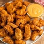 A plate of crispy, golden-brown chicken nuggets, inspired by a Chick-fil-A spicy nuggets recipe, sits next to a small bowl of creamy yellow dipping sauce.