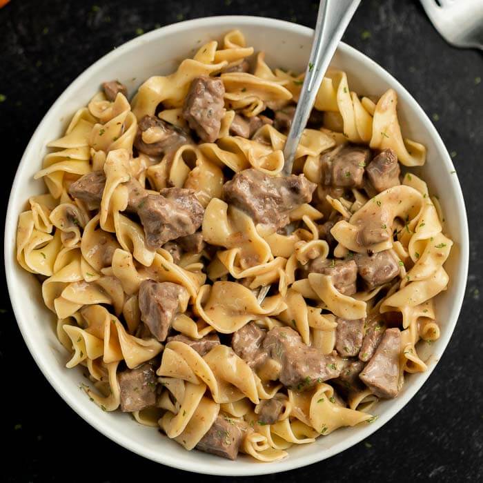 Close up image of a bowl of beef burgundy over noodles with a spoon. 
