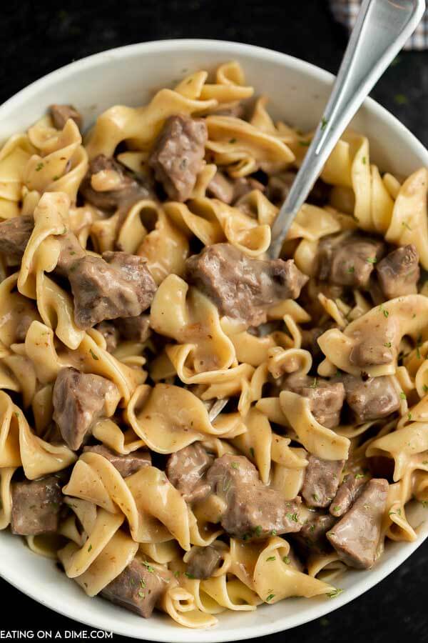 Close up image of a bowl of beef burgundy over noodles with a fork. 