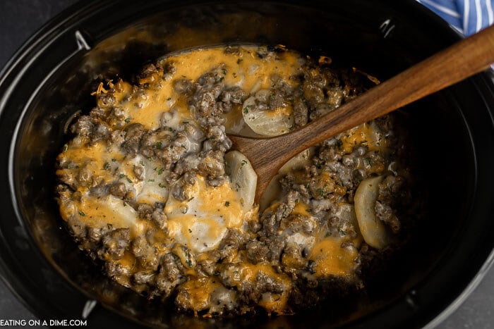 Close up image of crock pot hamburger potato casserole with a wooden spoon. 