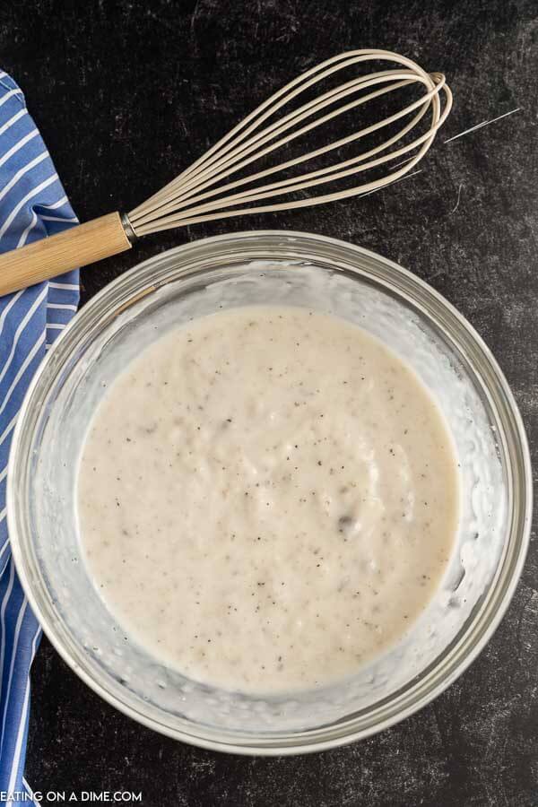 Combining the cream of mushroom soup with the milk and spices in a bowl with a whisk