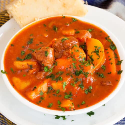 Bowl of Irish stew in a white bowl topped with fresh parsely.